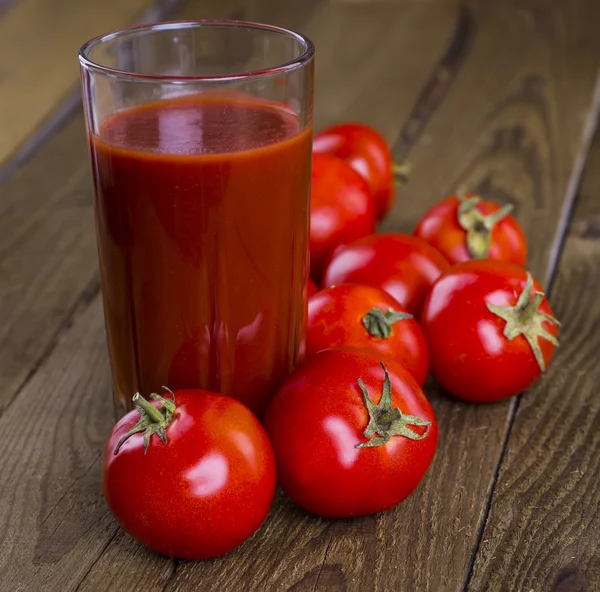 Bardak domates suyu ahşap ahşap masa üzerinde arka plan bitkiler
