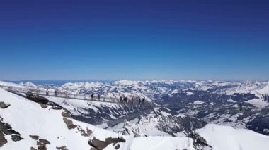 People Walking Across the Suspension Bridge on Glacier 3000 with Cable Car Station and Peak Walk in the Swiss Alps.