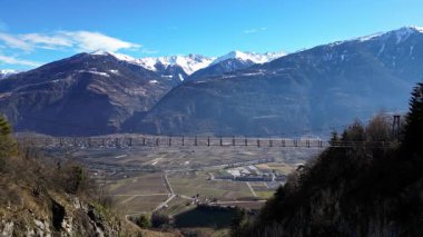 Passerelle Farinet üzerinden yürüyen turistler, güzel güneşli bir günde İsviçre Alpleri manzaralı Salentse Vadisi 'nin üzerindeki tahta köprü.