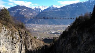 Passerelle Farinet üzerinden yürüyen turistler, güzel güneşli bir günde İsviçre Alpleri manzaralı Salentse Vadisi 'nin üzerindeki tahta köprü.