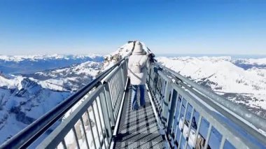 Buzul 3000, İsviçre - 15 Şubat 2025: Metal bir köprüde yürüyen genç bir kadın, Glacier 3000 'de iki tepe arasında asılı kaldı.