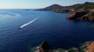 Esterel sahil şeridinin hava sinemasal manzarası turkuaz Akdeniz dalgaları, Fransız Rivierası, Güney Fransa manzaralı deniz manzaralı ve dramatik kızıl uçurumlar arasında seyreden bir sürat teknesi ile.