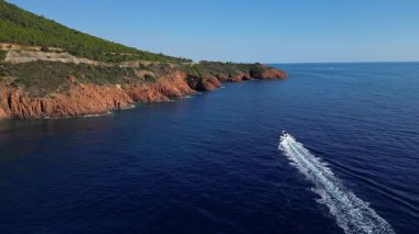 Esterel sahil şeridinin hava sinemasal manzarası turkuaz Akdeniz dalgaları, Fransız Rivierası, Güney Fransa manzaralı deniz manzaralı ve dramatik kızıl uçurumlar arasında seyreden bir sürat teknesi ile.