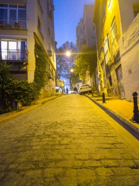 Alacakaranlıkta bir Türk şehrinde, sıcak sarı sokak lambalarıyla aydınlatılmış boş bir kaldırım taşı caddesi