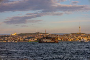 İstanbul Asya tarafında gün batımında camiler ve Camlica Kulesi ile denize açılan geleneksel Boğaz teknesi.