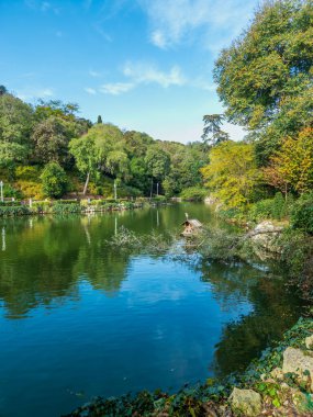 Açık mavi bir su ve arka planda ağaçlar olan bir göl. Ağaçlar yeşil ve gökyüzü mavi.