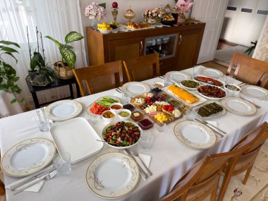 Uzun bir yemek masası, kutlama yemeği için bol yiyecek ve sofra takımı ile cömertçe hazırlanır..
