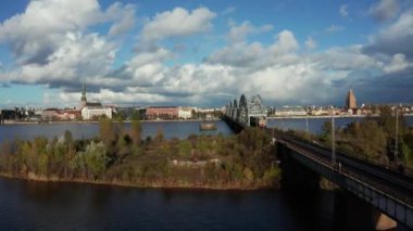 Riga 'daki Daugava nehrinin üzerinden eski kasabaya doğru uçuyor. Şehre giden ve giden tren köprüsü. Aerial Riga videosu, Letonya 'nın başkenti.