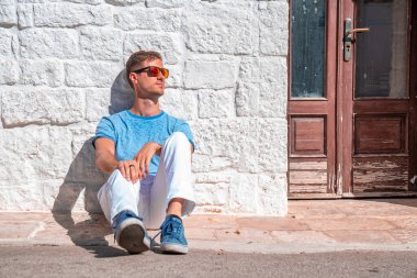 İtalya 'nın Puglia bölgesindeki Bari eyaletinin Alberobello kentindeki trulli evlerin yanında oturan genç adam. Güzel İtalya, Bari bölgesi.