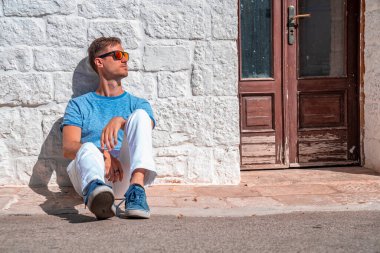 İtalya 'nın Puglia bölgesindeki Bari eyaletinin Alberobello kentindeki trulli evlerin yanında oturan genç adam. Güzel İtalya, Bari bölgesi.