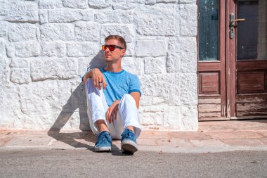 İtalya 'nın Puglia bölgesindeki Bari eyaletinin Alberobello kentindeki trulli evlerin yanında oturan genç adam. Güzel İtalya, Bari bölgesi.