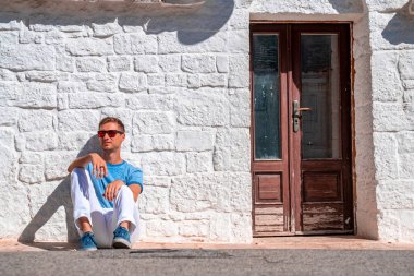 İtalya 'nın Puglia bölgesindeki Bari eyaletinin Alberobello kentindeki trulli evlerin yanında oturan genç adam. Güzel İtalya, Bari bölgesi.