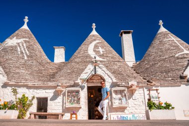 Genç adam, İtalya 'nın Puglia bölgesindeki Bari eyaletinin Alberobello kentindeki geleneksel trulli evlerinin yanında duruyor. Güzel İtalya, Bari bölgesi.