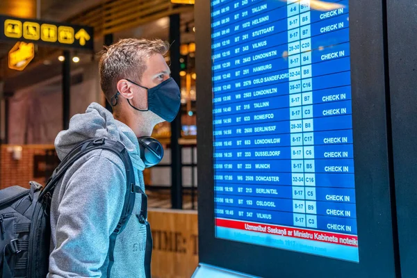 Banner photo of young man wearing face mask with suitcase checking flight cancellation status on airport information board in empty airport. Airline bankrupt, airline crisis or new normal concept