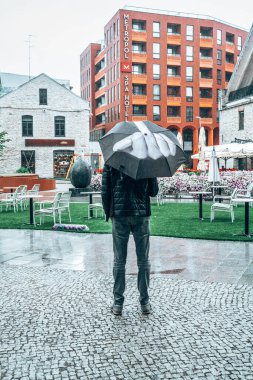 Tallinn, Estonya. 10 Haziran 2020. Öfkeli öfkeli adam şemsiyesini tutuyor ve orta parmağı havada yağmuru işaret ediyor..