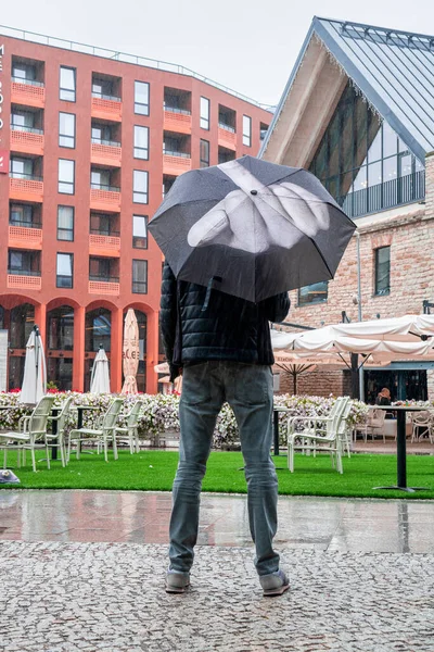 Tallinn, Estonya. 10 Haziran 2020. Öfkeli öfkeli adam şemsiyesini tutuyor ve orta parmağı havada yağmuru işaret ediyor..