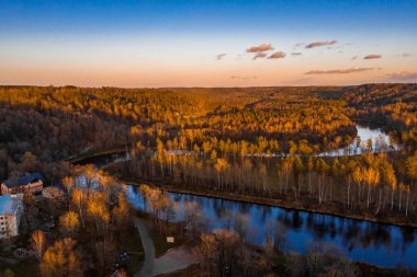 Sonbahar renklerinde sık ormanı geçen kıvrımlı nehir manzarası.