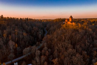 Letonya, Sigulda 'da gün batımında Turaida kalesi ve Gauja nehri havadan görülüyor. Kalenin yanında turuncu orman ve nehirle altın sonbahar.