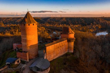 Letonya, Sigulda 'da gün batımında Turaida kalesi ve Gauja nehri havadan görülüyor. Kalenin yanında turuncu orman ve nehirle altın sonbahar.