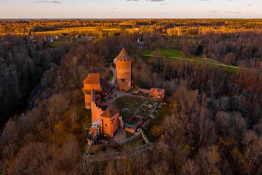 Letonya, Sigulda 'da gün batımında Turaida kalesi ve Gauja nehri havadan görülüyor. Kalenin yanında turuncu orman ve nehirle altın sonbahar.