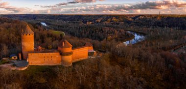 Letonya, Sigulda 'da gün batımında Turaida kalesi ve Gauja nehri havadan görülüyor. Kalenin yanında turuncu orman ve nehirle altın sonbahar.