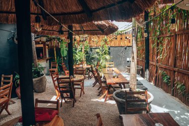 Boş ahşap sandalyeler ve açık kafede saman şemsiyeli masalar.