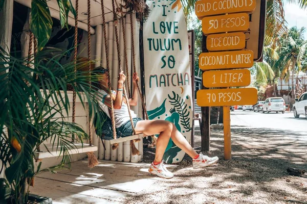 Mujer sentada en el columpio de la tienda de coco con menú de bebidas al borde de la carretera — Foto de Stock