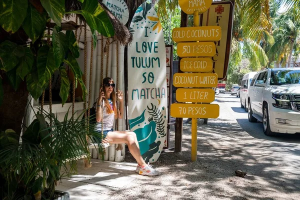 Mujer sentada en el columpio de la tienda de coco con menú de bebidas al borde de la carretera — Foto de Stock