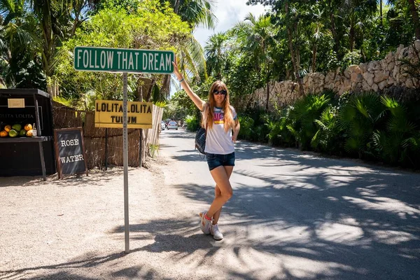 Beautiful female tourist leaning on motivational sign at roadside — Stock Photo, Image