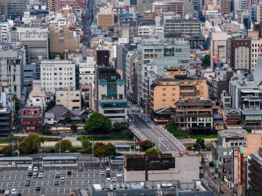 Japonya 'nın Kyoto kentinin havadan görünüşü, bir nehir, yeşillik, modern ve geleneksel binalar, merkezi bir yol ve ön planda bir otopark gösteriyor..