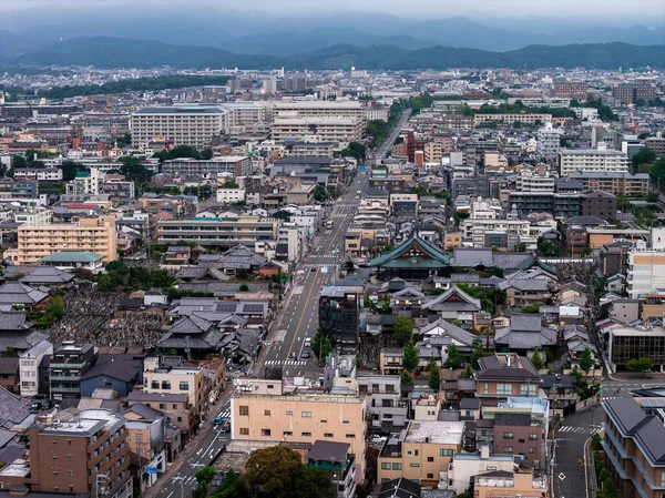 Japonya 'nın Kyoto kentinin hava manzarasında yeşil çatılı büyük bir tapınak, geleneksel binalar, dar sokaklar ve bulutlu gökyüzünün altında dağlık bir ufuk var..