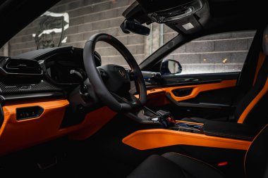 Lamborghini Urus 'un içini kapatın. Karbon fiber detaylar, turuncu dikişler, İtalyan bayrağı amblemi ve Lamborghini logosu olan beton bir duvar..