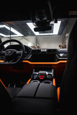Lamborghini Urus 'un içini kapatın. Siyah ve turuncu gösterge paneli, Lamborghini amblemi, fütüristik kontroller ve kırmızı kontak anahtarı..