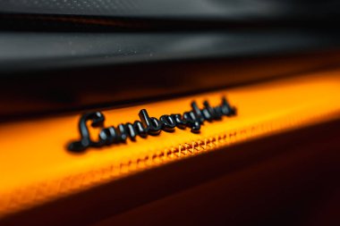 Lamborghini logosu parlak turuncu desenli bir yüzeyde, logoya keskin bir odaklanmayla ve kontrastlık için bulanık bir arka planda sergileniyor..