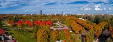 Riga, Letonya 'daki Zafer Parkı' nda altın sonbahar yaprakları görünür yollar ve Ulusal Kütüphane ve yüksek binaların yer aldığı şehir silueti..