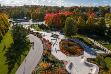 Riga, Letonya 'daki Zafer Parkı' nın sonbahar manzarası. Canlı altın ve kırmızı ağaçlar modern bir kaykay parkının etrafında insanların parkın tadını çıkardığı bir yer..