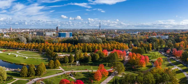 Riga, Letonya 'daki Zafer Parkı' nın havadan görünüşü, altın sonbahar yaprakları, dolambaçlı yollar, bir çeşme ve ufukta Riga TV Kulesi yer alıyor..