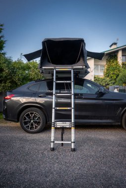 Çatı üstü açık, merdiven merkezli çakıllı yol kenarındaki siyah lüks SUV parkları. Akşam ışığında, modern bir ev ve bahçenin yakınında alçak çekim yapın..