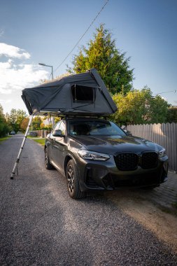 Lüks bir SUV, banliyö çakıl yolu üzerinde, çatısı ve alüminyum direği olan, bahçe çitleri ve sokak lambası olan, üç çeyrek açılı, karanlık bir arazi aracı parkı..