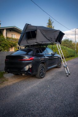 Kıyıya yakın sakin bir banliyö caddesinde siyah lüks bir SUV park ediyor. Yukarısında merdiveni aşağıda, sert, kabuklu bir çatı çadırı var. Öğleden sonra ışığı sakin ve lüks bir seyahat havası katıyor..