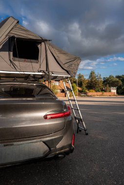 Çatıda çadırı ve tentesi olan lüks bir SUV kıyı şeridinde duruyor. Bir alüminyum merdiven çadıra ulaşır. Sıcak kenar ve bulutlar öğleden sonra havasını tanımlar..