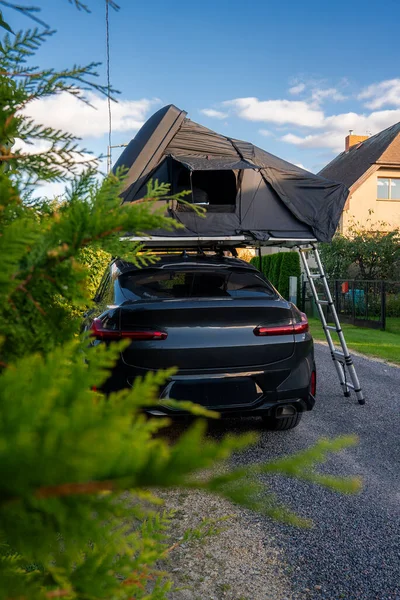 Çitlerin ve şeftali evin yanına park etmiş, çatısı ve merdiveni olan koyu renkli bir SUV. Öğleden sonra ışığı ve yumuşak ön plan yaprakları hazır bir kaçış sahnesi oluşturur..