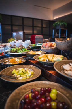 Shallow bowls of fresh fruit, salads, and cold dishes sit on wooden risers in a modern Japan hotel dining room, warm light and shallow depth of field present