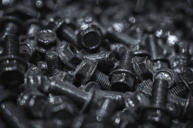 Close macro shows black bolts and hex head screws, threads gleam under harsh industrial light. Tight composition, shallow depth of field, metallic texture stands out.