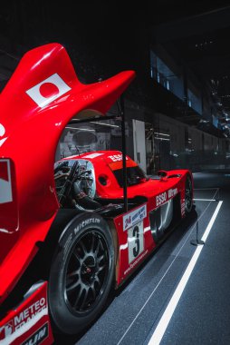 3 numaralı kırmızı bir Toyota dayanıklı araba Japonya 'da karanlık bir müzenin arkasında duruyor, dikiz manzarası büyük kuyruk yüzgeci, Japon bayrağı, Esso ve Michelin logolarını gösteriyor..