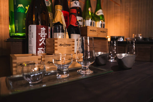 Warm bar counter in Japan presents kanji sake bottles, wooden masu, and clear glasses on a tray, with dark wood, soft ambient light, and connoisseur focused details.