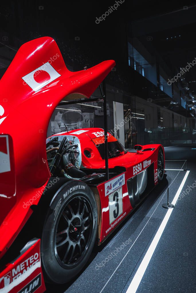 A red Toyota endurance car with number 3 sits behind stanchions in a dark museum in Japan, rear quarter view shows large tail fin, Japanese flag, Esso and Michelin logos.