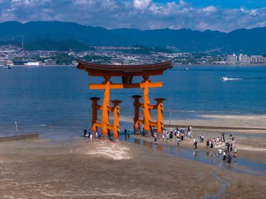 Hava görüntüsü, Hiroşima yakınlarındaki Miyajima 'daki gelgit düzlüklerinde Büyük Torii' yi gösteriyor. Ziyaretçiler, mavi Seto İç Denizi 'nde ve şehir merkezinde gün ortasında dağlarla birlikte yürüyorlar..