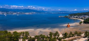 Hava görüntüsü Miyajima 'nın Büyük Torii ile alçak sularda, sığ sularda, kumlu düzlüklerde ve Hiroşima kıyılarında olduğunu gösteriyor. Gün ortası ışığı, derin mavi su ve dağınık bulutlar..