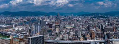 Japonya, Hiroşima 'nın hava görüntüsü şehir şebekesini, yüksek demiryollarını ve Ota Nehri kanallarını gün ortası ışığı altında gösteriyor. Orta ve yüksek binalar uzak dağlarla çevrili bir havzayı doldurur..